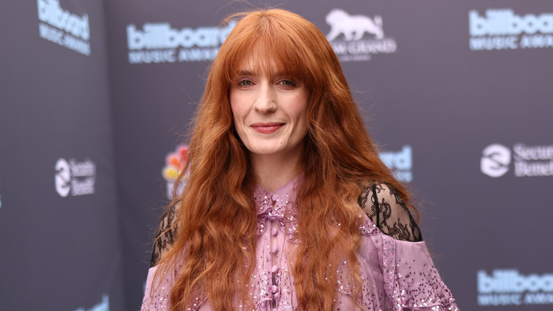 Florence Welch smiles at a red carpet event while wearing a light pink dress with lace sleeves