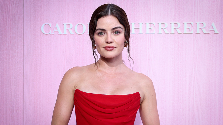 Lucy Hale wears a red strapless gown while posing in front of a pink background