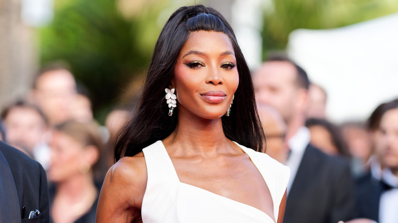 Naomi Campbell wears a white dress and a full glam makeup look at an outdoor event