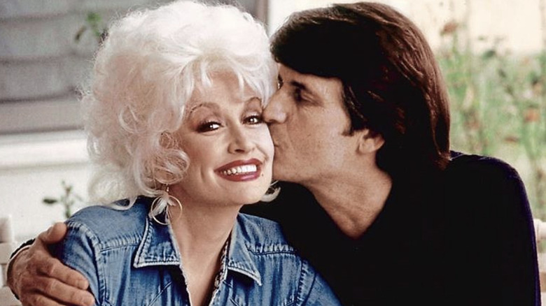 Dolly Parton in a denim jacket receiving a kiss on the cheek from her late husband Carl Dean.