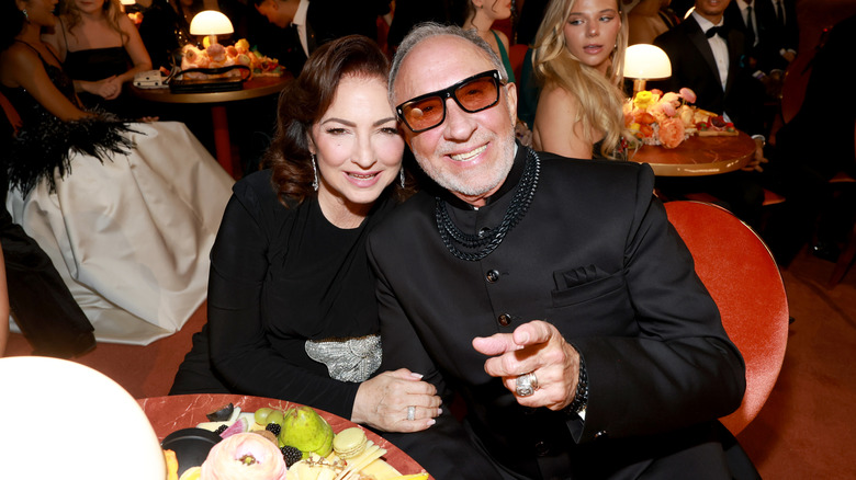 Gloria Estefan in a black gown, sitting next to her husband Emilio Estefan dressed in all black.