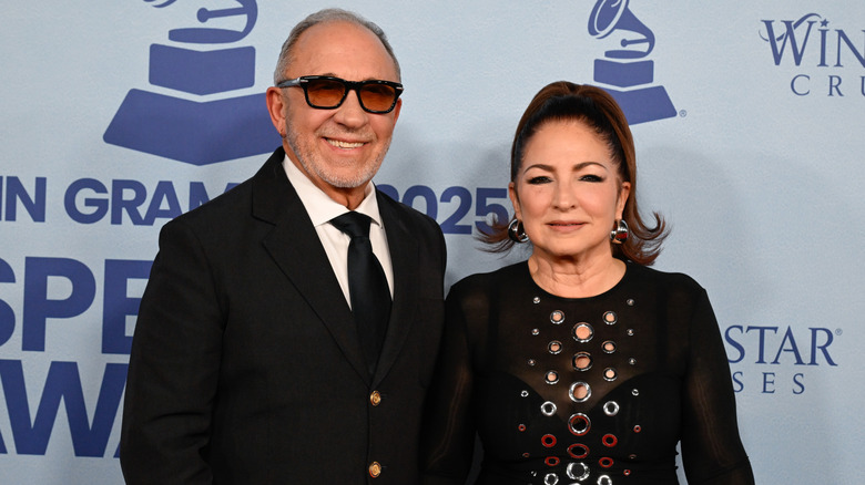 Gloria Estefan in a black and silver dress with her hair in a ponytail standing next to Emilio Estefan wearing a black suit.
