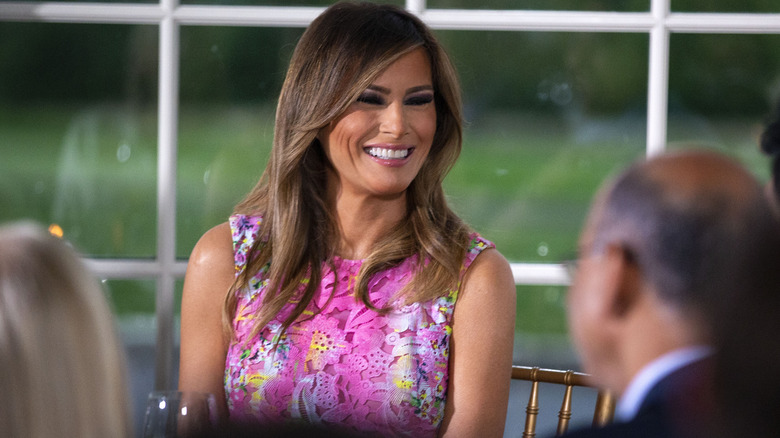 Melania Trump smiling in a pink lace dress with florals