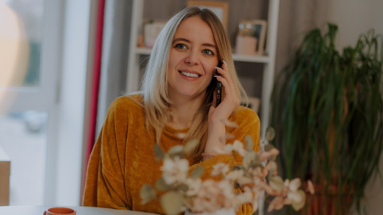 A woman wearing a mustard yellow sweater while talking on the phone