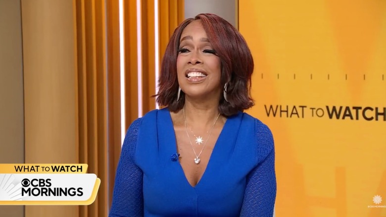 Gayle King smiling wearing a royal blue dress with two pendant necklaces.
