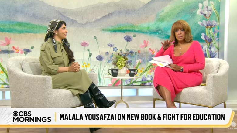 Gayle King wearing a pink dress interviewing Malala Yousafzai wearing a green and black ensemble.