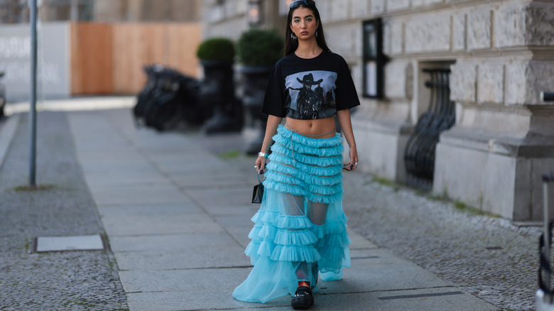 A woman in a sheer skirt, crop top, and Crocs