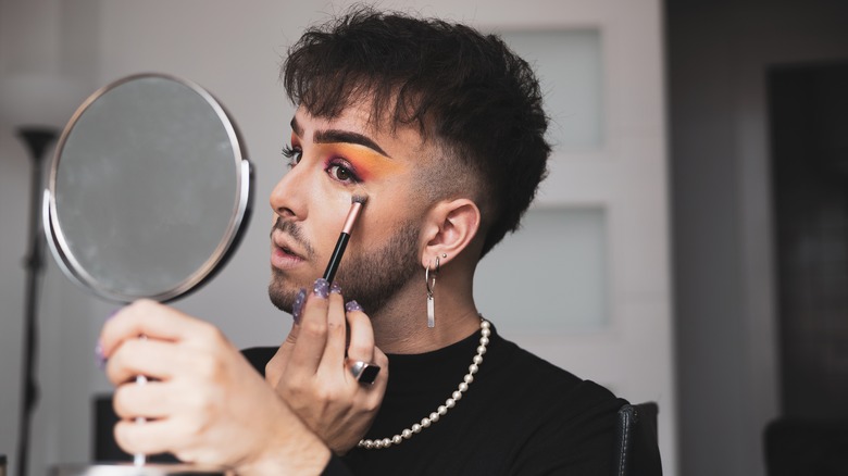 Man applying makeup in mirror