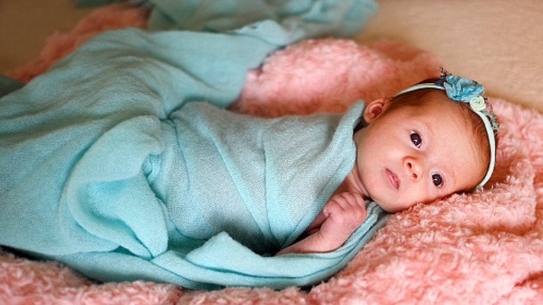 A baby wrapped in a blue blanket lying on a pink comforter