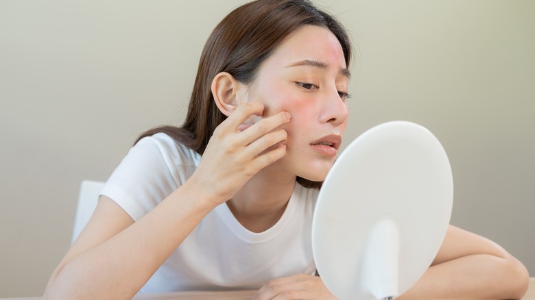 Woman examines skin in mirror 