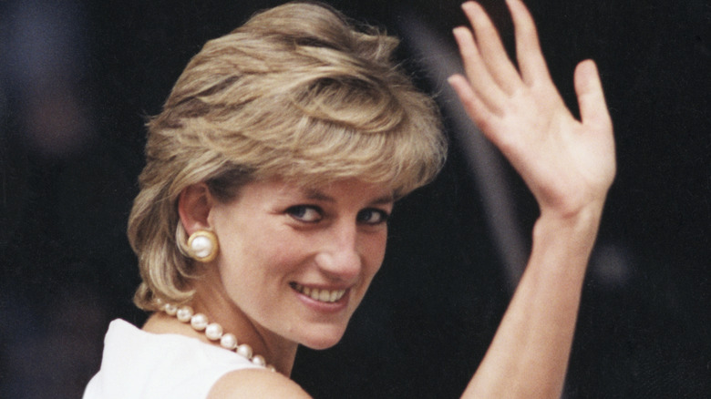 Princess Diana waving in Chicago wearing a white dress and pearl jewelry.