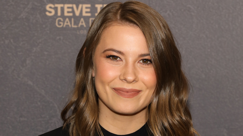 Bindi Irwin wears a soft-glam makeup look with soft peach-colored lipstick and loose waves in her hair.