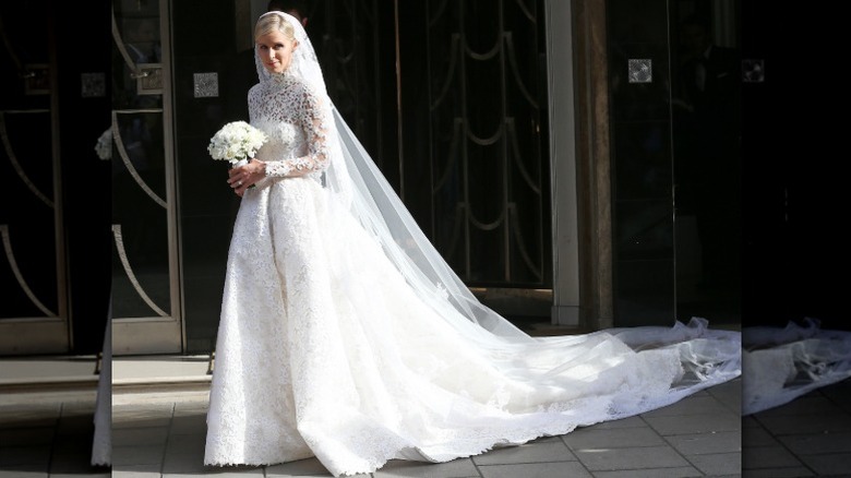 Nicky Hilton holding a bouquet on her wedding day in a ball-gown dress with a long train.
