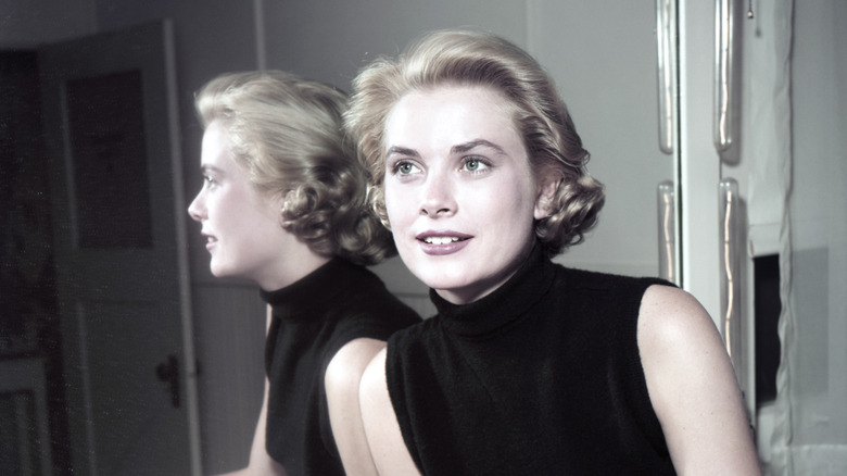 Grace Kelly wearing a black sleeveless top in front of a mirror.