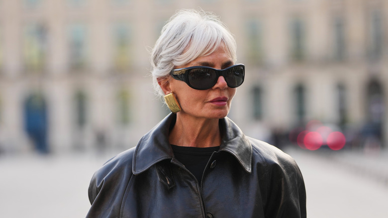 A woman poses wearing a black leather jacket and black sunglasses