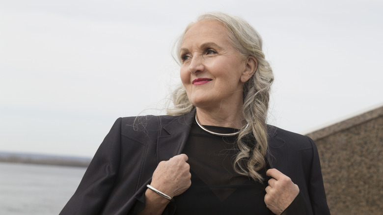 A woman wearing a black shirt and jacket with warm highlights in her curly gray hair.