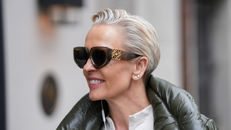 A woman wearing sunglasses and a puffer jacket with short gray hair and warm highlights.