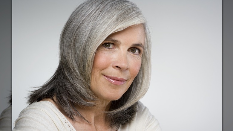 A woman smiles with a gray side part