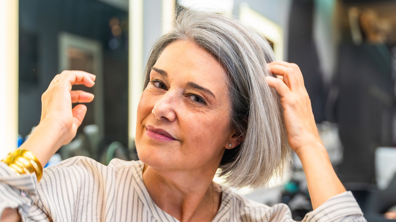 A woman adjusting her gray side-part lob