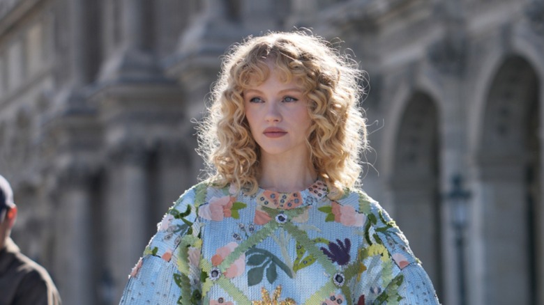 A woman with blond curls wears a patterned dress