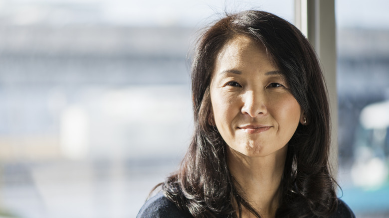 A woman with shoulder-length layered hair looking content as she stares at the camera in front of a window.