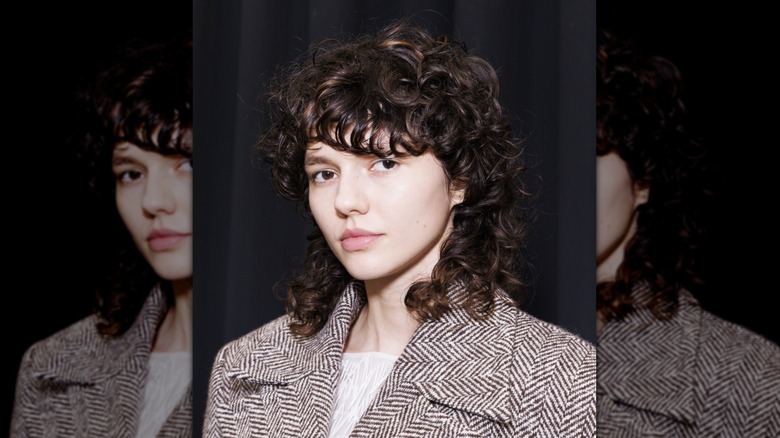 A person with a brown curly wolf cut