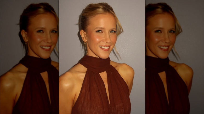 Jessy Schram smiling wearing a brown dress and an updo
