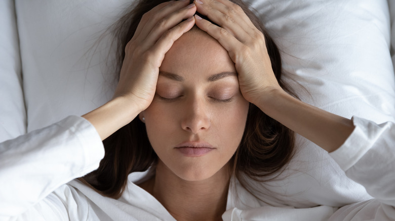 Woman holding head in bed