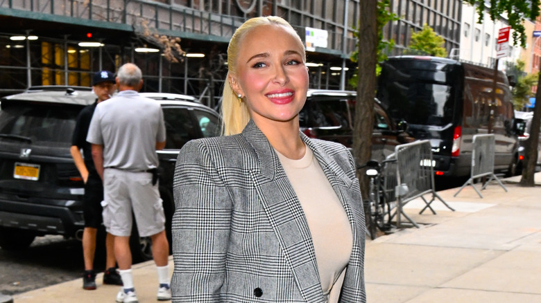 Hayden Panettiere walking outside wearing her hair in a ponytail and a black and white plaid blazer
