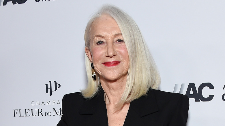 Actor Helen Mirren smiles while black blazer and red lipstick at an event.
