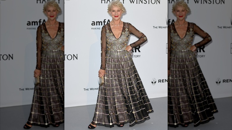Helen Mirren posing with her hand on her hip at an event in 2016 wearing a detailed black and silver gown.