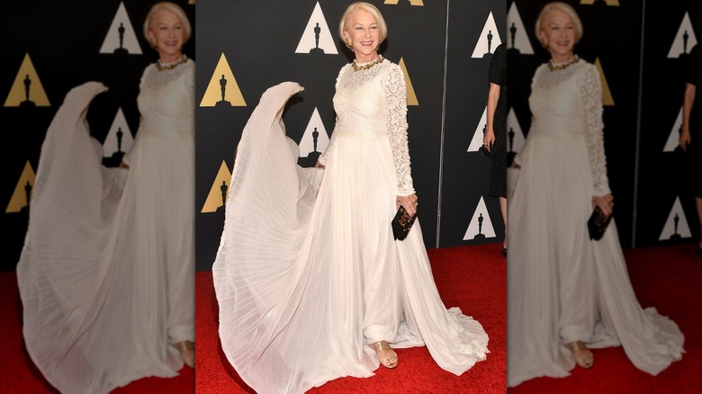 Helen Mirren smiling on the red carpet in 2015 wearing a white dress with a flowing skirt.