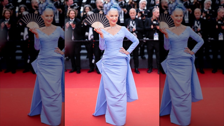 Helen Mirren holding a fan on the red carpet in 2023 wearing a periwinkle dress and matching hair.