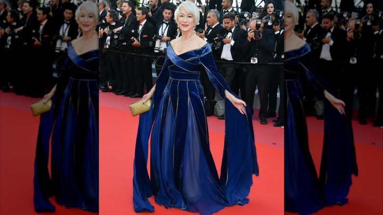 Helen Mirren posing on the red carpet in 2018 wearing a regal blue velvet gown with long flowing sleeves.