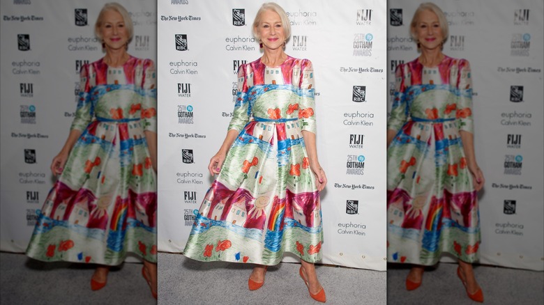 Helen Mirren posing at an event in 2015 wearing a colorful dress with orange shoes.