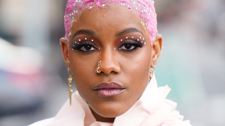 woman with magenta hair, makeup, and a nose piercing poses for a photo