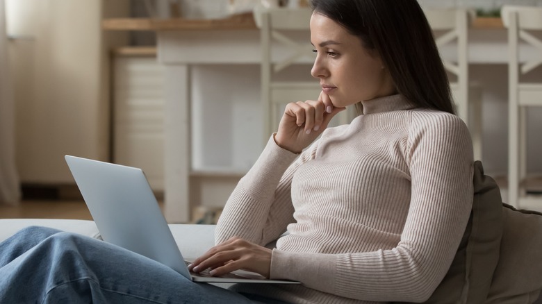 young woman laying on couch staring at computer