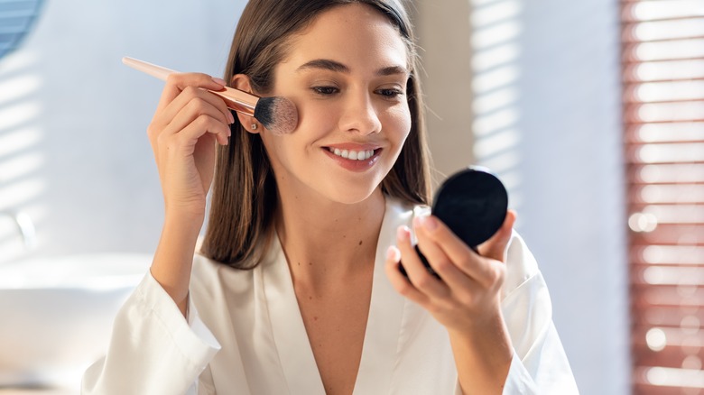 Woman applies blush with makeup brush