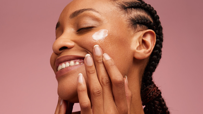 Woman applying skincare to cheeks while smiling 