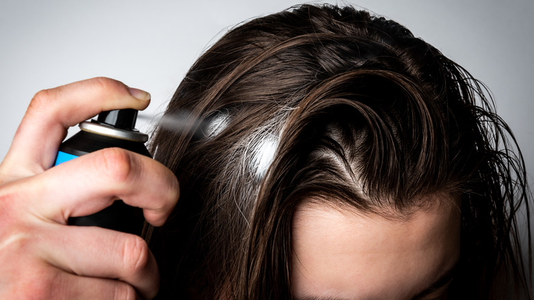 Person spraying aerosol dry shampoo to roots of hair