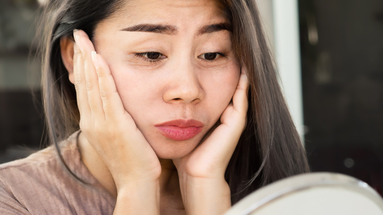 Woman looking at under-eye circles in mirror