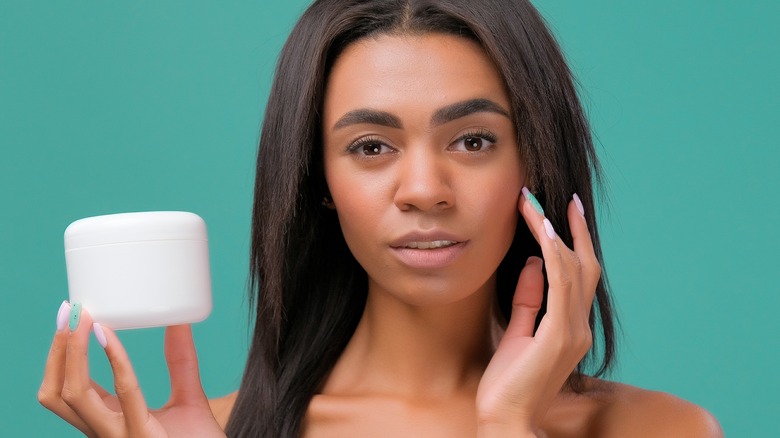 woman holding a jar while rubbing cream onto her face