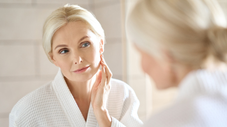 older woman looking in mirror at her face