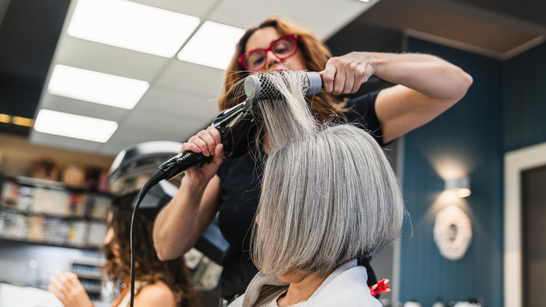 Woman with a gray bob in a salon having her hair styled with a blow dryer and brush.