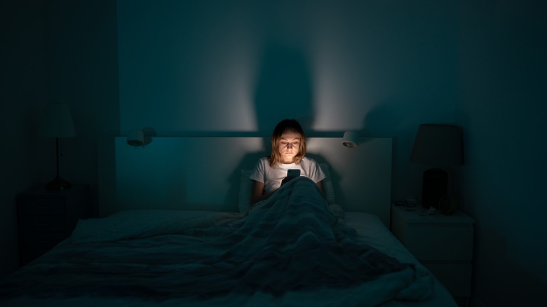 Woman scrolls phone in bed