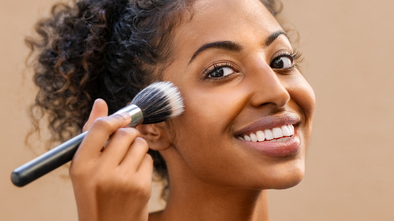 curly-haired woman applying bronzer