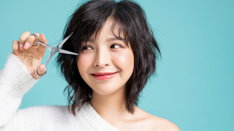 Asian woman cutting her own bangs