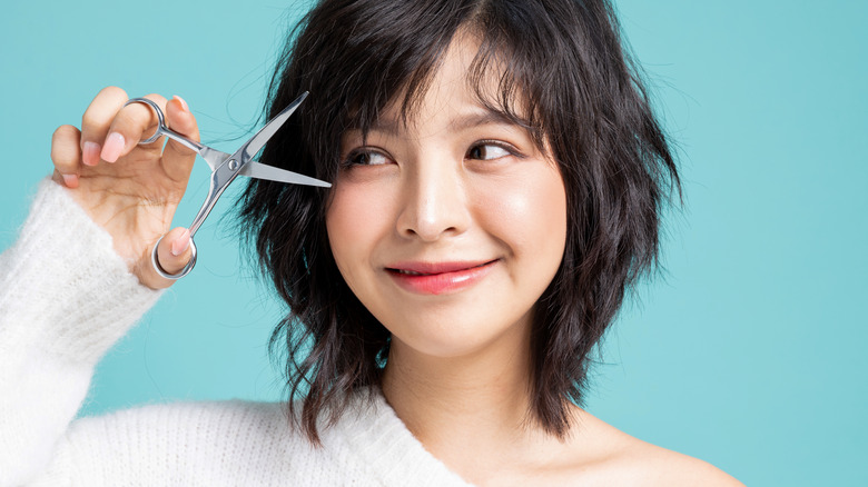 Asian woman cutting her own bangs