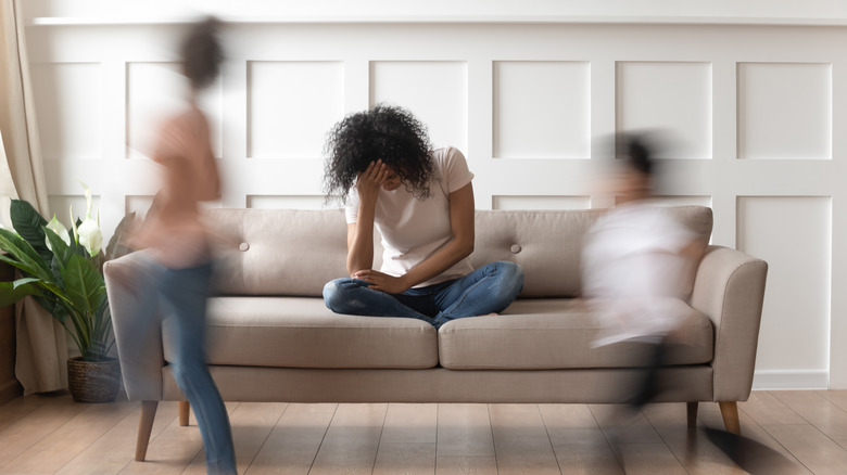 mom sitting on couch as kids run around