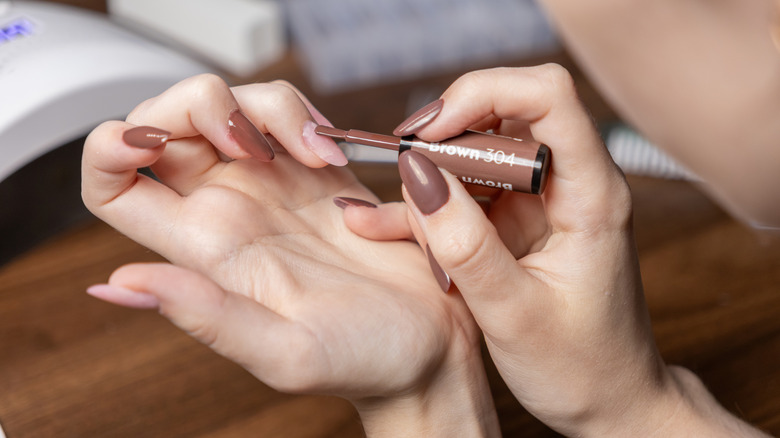 A person doing their own gel manicure with an LED lamp in the background